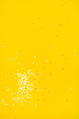 Tiny pearl stars on yellow background. Flat lay, top view.