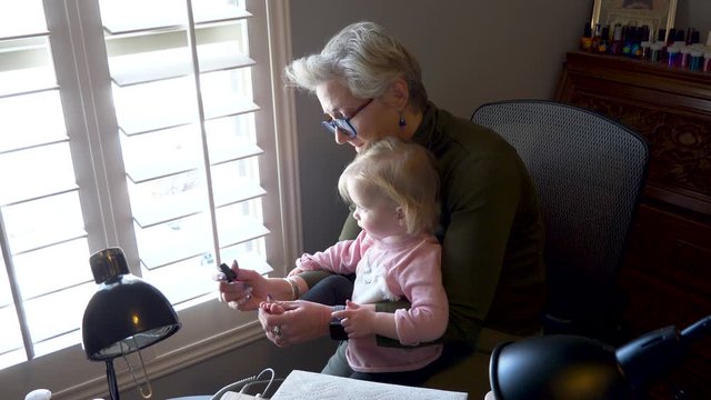 Tender and gentile grandmother painting the toenails of her toddler grandchild in a home salon