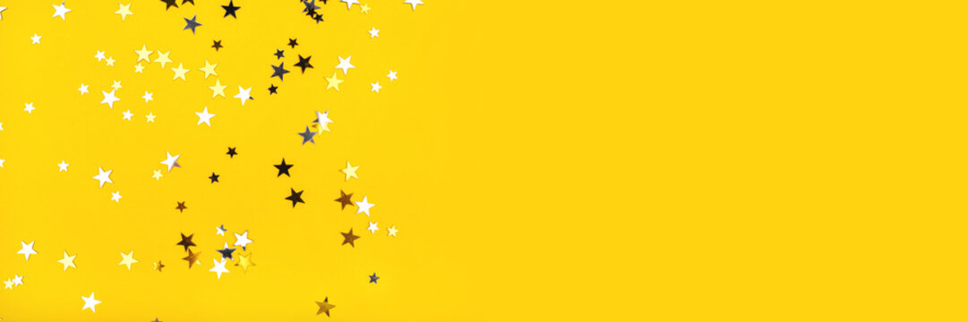 Golden and silver stars on yellow background. Flat lay, top view.