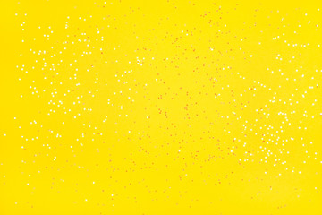 Tiny pearl stars on yellow background. Flat lay, top view.
