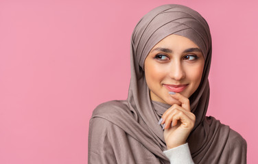 Smiling muslim woman in hijab thinking about something and looking aside