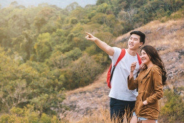 Happy romantic Couple Man and Woman travel and trek at asia tropical forest. Man backpacker hand up and pointing to destination on top of mountain, Landscape background. Adventure concept.