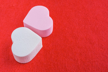 pink and white pastel cosmetic sponges in heart shape on red felt background.