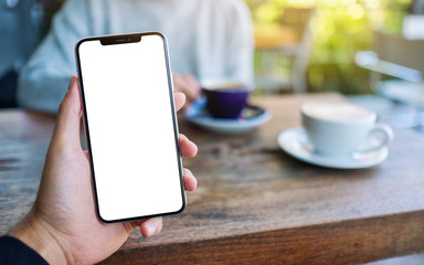 Mockup image of a man holding black mobile phone with blank white screen with woman drinking coffee in cafe