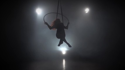Silhouette young caucasian brunette sportive dancer female balancer in beige leotard back lying hang on aerial hoop on three rays of light background. Slow motion. 068