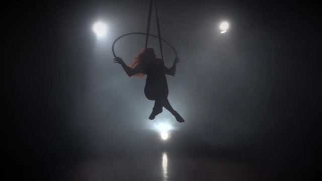 Silhouette young caucasian brunette sportive dancer female balancer in beige leotard back lying hang on aerial hoop on three rays of light background. Slow motion. 068