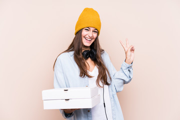 Young caucasian woman holding pizzas isolated joyful and carefree showing a peace symbol with fingers.