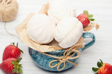 White-pink marshmallows with fresh strawberries in a blue cup tied with a scourge on a white background