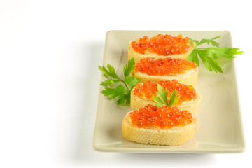 Slices of white loaf with red caviar and parsley on the white dish and on the white background.