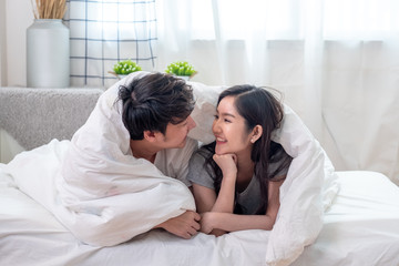 Lovely young couple covered with white blanket on white bed in bed room looking into eyes each other. Lovely couple romantic concept