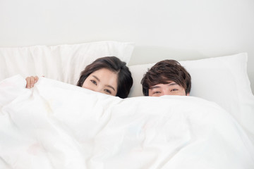 Lovely young couple covered with white blanket on white bed in bed room looking into eyes each other. Lovely couple romantic concept