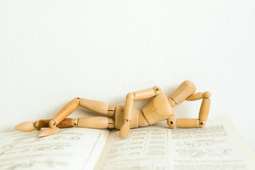 Wooden mannequin manikin lie down and rest on an open book. He is thinking of mastering the...