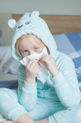 child with cold symptoms in a blue cute home jumpsuit on a large bed