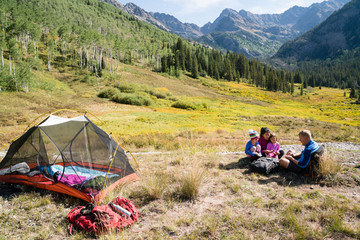 Family playing cards and relaxing while on backpacking trip with beautiful views in thh background.