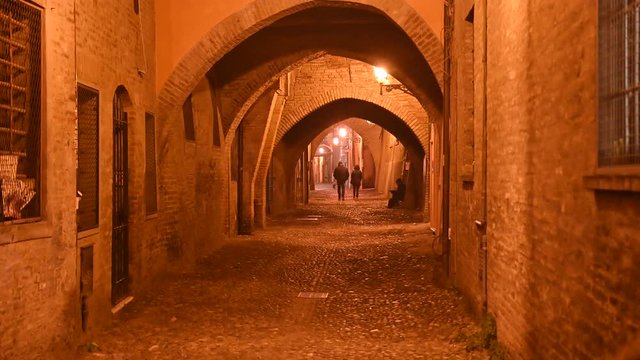 Ferrara, Italy. December 2019. Night footage of the Via delle arcate: characterized by the cobbled street and arches. Ancient street that maintains its medieval charm. A couple stroll.
