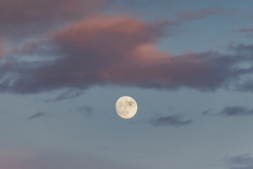 moon at sunset in a light sky with orange clouds