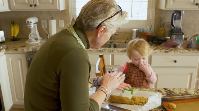 Loving and tender grandmother making cookies with granddaughter toddler - baby girl mostly just eating the cookie dough
