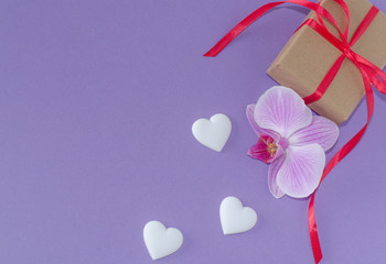 Gift box, orchid flower and white hearts on a violet background. Valentine's day and romantic concept. Flat lay. Copy space.