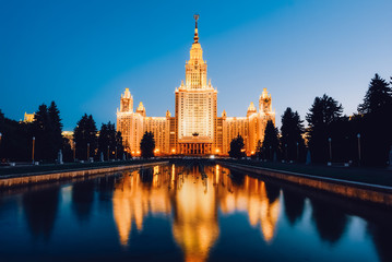 Fototapeta na wymiar Moscow State University in golden light against a blue sky with reflections in the water