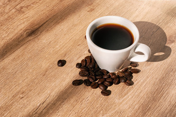 coffee cup next to coffee beans, on wooden surface, diagonal view