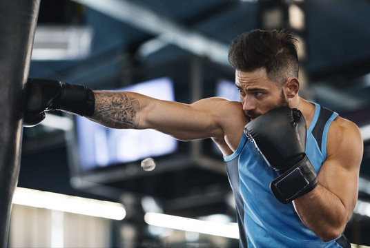 Active sportsman training with boxing bag at gym