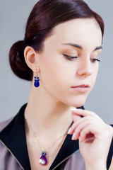 Fototapeta premium Closeup Portrait of Beautiful Caucasian Lady with Blue Pendant and Earring. Against Gray.