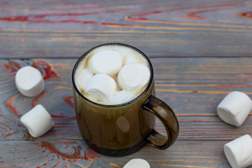 Marshmallow. Retro style wooden background. Glass mug with marshmallow in it. There is also a woolen scarf. Close-up. Tinted