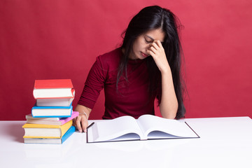 Exhausted Asian woman got headache read a book with books on table.