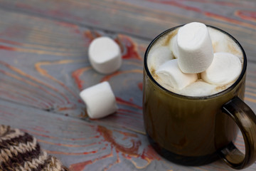 Marshmallow. Retro style wooden background. Glass mug with marshmallow in it. There is also a woolen scarf. Close-up. Tinted