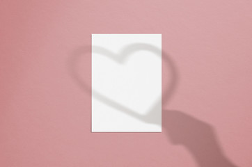 Blank white vertical paper sheet 5x7 inches with hand and heart shadow overlay. Modern and stylish valentine greeting card or wedding invitation mock up.