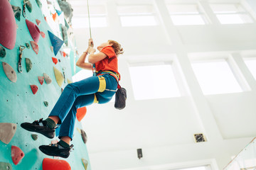 Teenager boy at indoor climbing wall hall. Boy is climbing using a top rope,chalk bag and climbing harness. Active teenager time spending concept image.