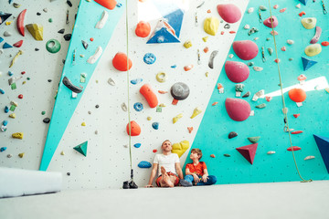 Father and teenager son sitting near the indoor climbing wall. They resting after the active...