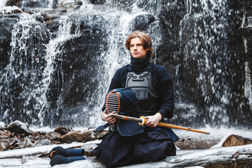 Man practicing kendo with bamboo sword on waterfall background. Place for text or advertising