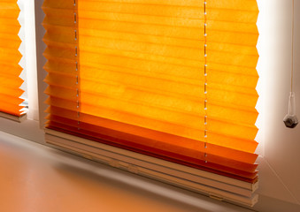 Pleated blinds with orange folded fabric on the window close up. Cordless bottom up top down...