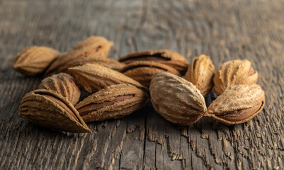 Inshell almonds on a background of rough wood texture. Selective focus.