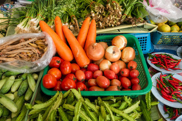 Vegetables in red and orange of tomato, carrot and onion surround with green vegetables for sale in fresh market.
