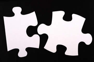 Two white big puzzles on a black background. Empty space. Concept in business