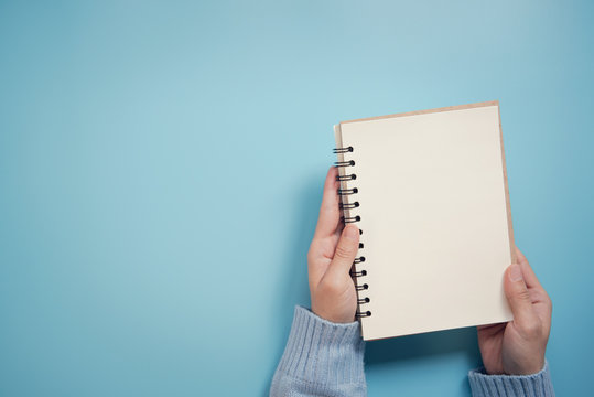 Female Hands Holding Closed Book With Blank Cover On Blue Background