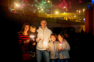 Beautiful new year family portrait of happy children and parents celebrating New Year together and lighting sparklers outdoors