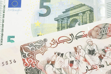 A beige, two hundred Algerian dinar bill with a red, European Union five euro bank note close up in macro