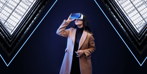 Beautiful woman in fashionable clothes over geometric dark background. Girl in glasses of virtual reality. Augmented reality, game, future technology concept. VR. 