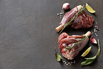 Raw lamb shanks with herbs and spices. Flat layot on dark concrete background. Copy space