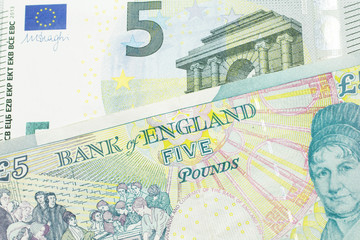 A five pound British pound sterling with a red, five Euro European bank note close up in macro