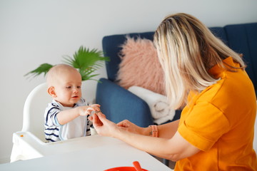 Mom feeding her baby girl with a spoon. Mother giving food to her eight-month child at home.