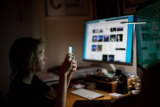 Boy looking at smart phone in the dark in front of computers
