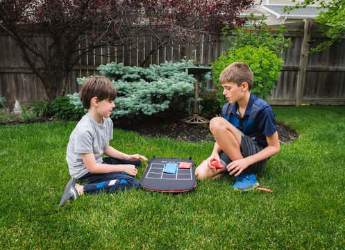 Two young boys playing a tic tac toe game in the backyard together.