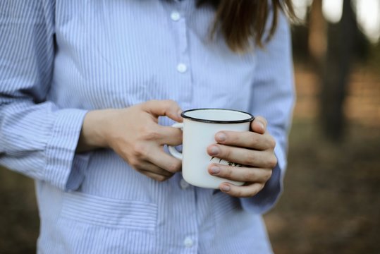Outdoors shot of a hand of person holding a white metal cup