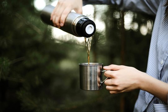 Close-up of woman pouring tea from insulated drink container int