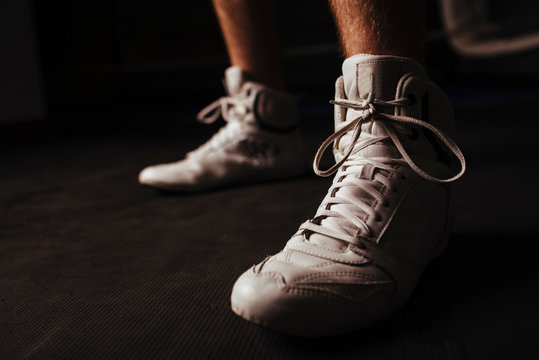 Closeup of white boxing shoes on dark background during workout.