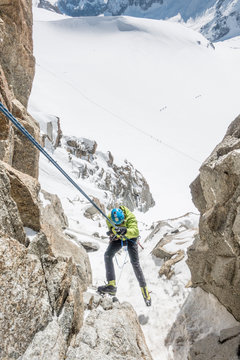 An alpinist is on rappel in steep terrain high above a French glacier